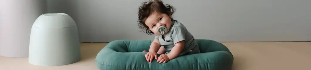 Baby sitting on a green lounger with pacifier, modern nursery setting