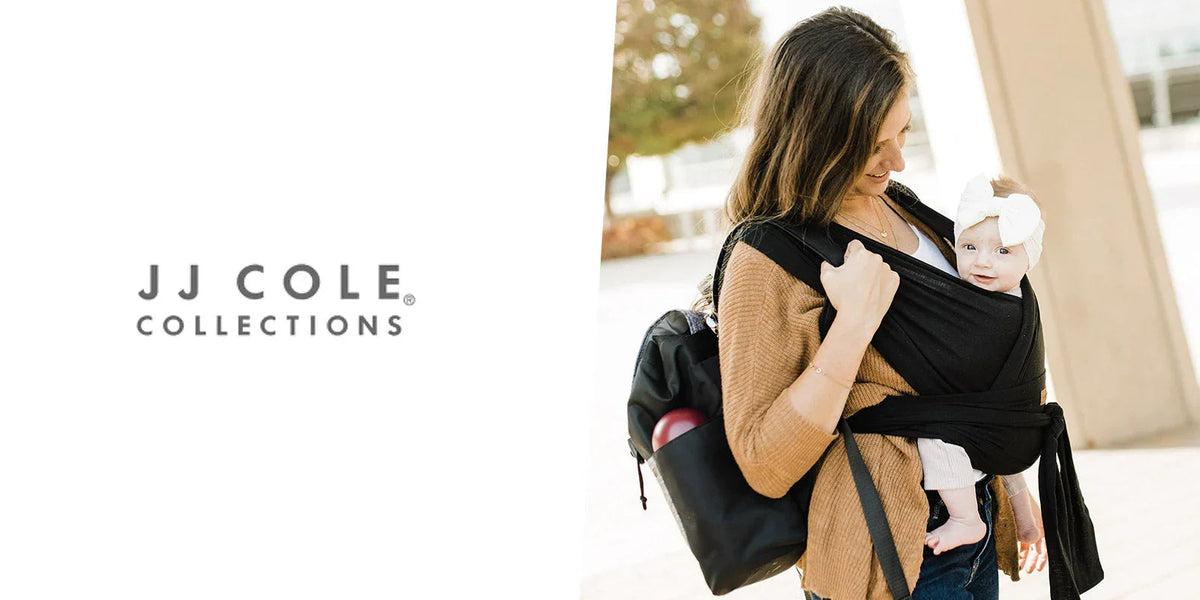 Woman outdoors carrying baby in black wrap carrier, wearing backpack, baby in white headband
