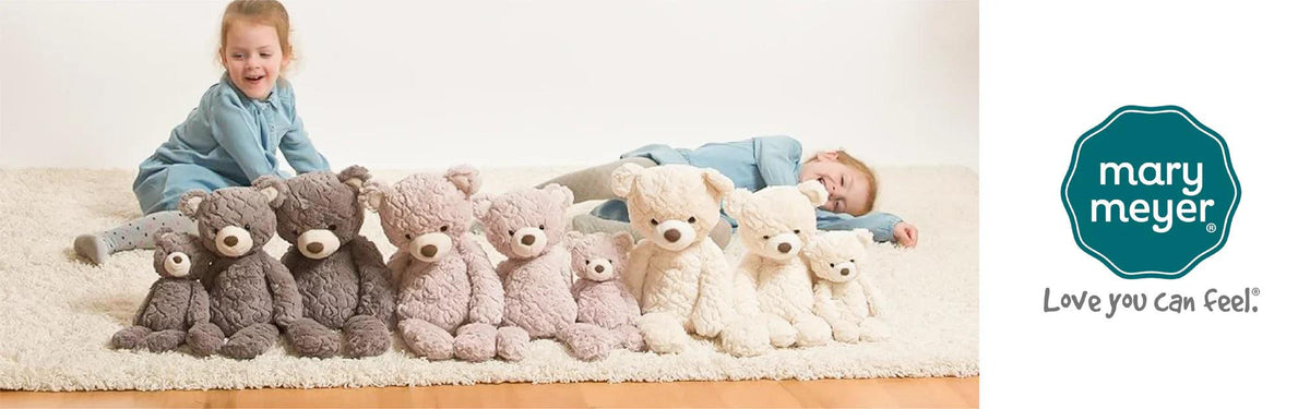 Two children in blue outfits playing with plush teddy bears in various colors and sizes on a soft rug
