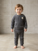 Toddler wearing a grey ribbed lounge set with a smiley face patch, standing indoors on a plain floor.