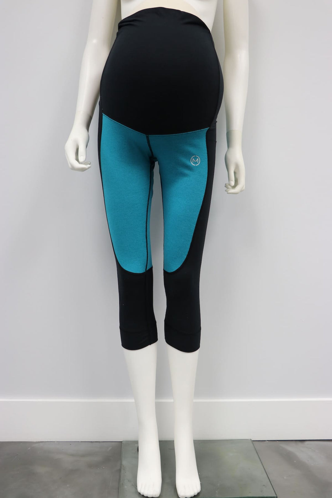 Teal and black maternity leggings displayed on a mannequin against a plain wall.
