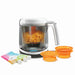 Baby Brezza food maker with diced vegetables inside, two orange bowls, and reusable baby food pouches.