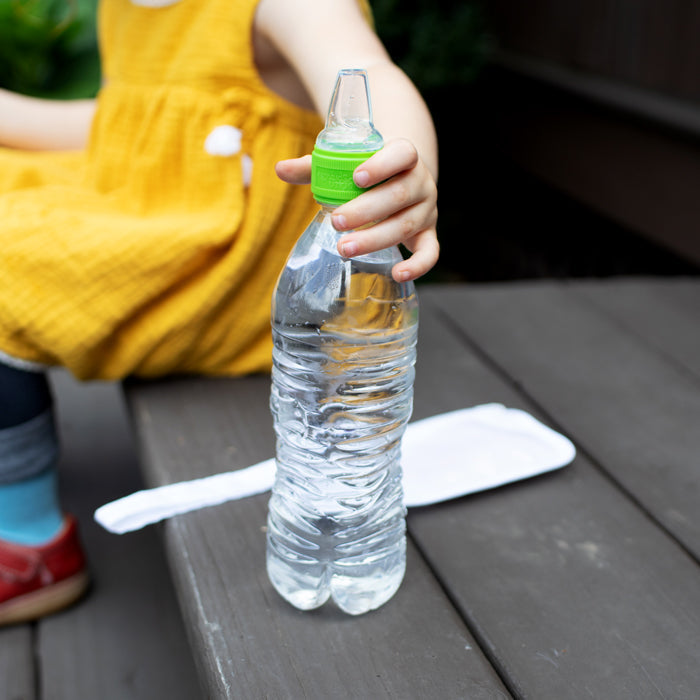 Spout adapter for water bottle held by a child sitting outdoors on a wooden bench.