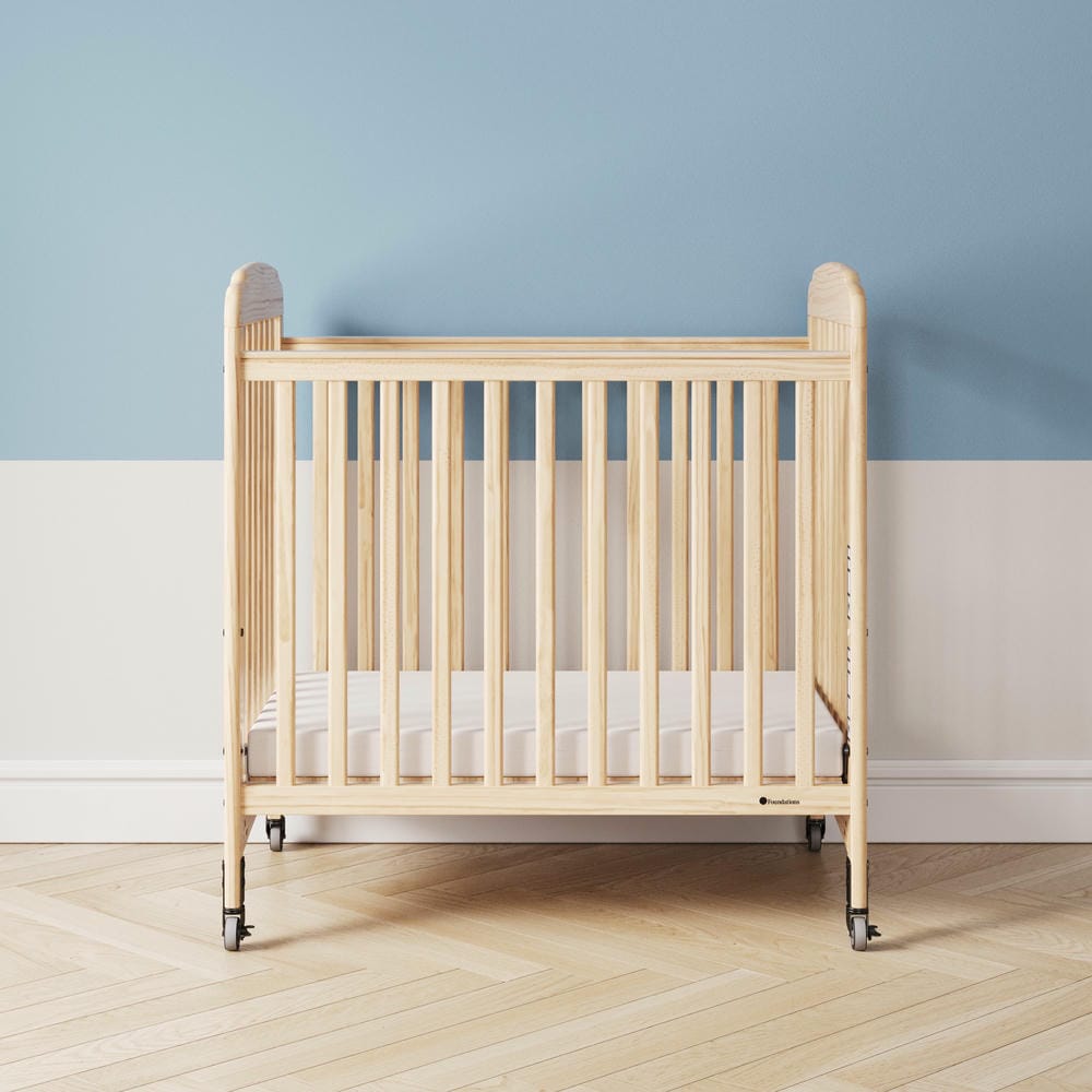Natural wood baby crib with wheels in a modern nursery with blue and white wall