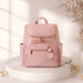 Light pink diaper backpack with gold zippers on display pedestal, baby toy nearby