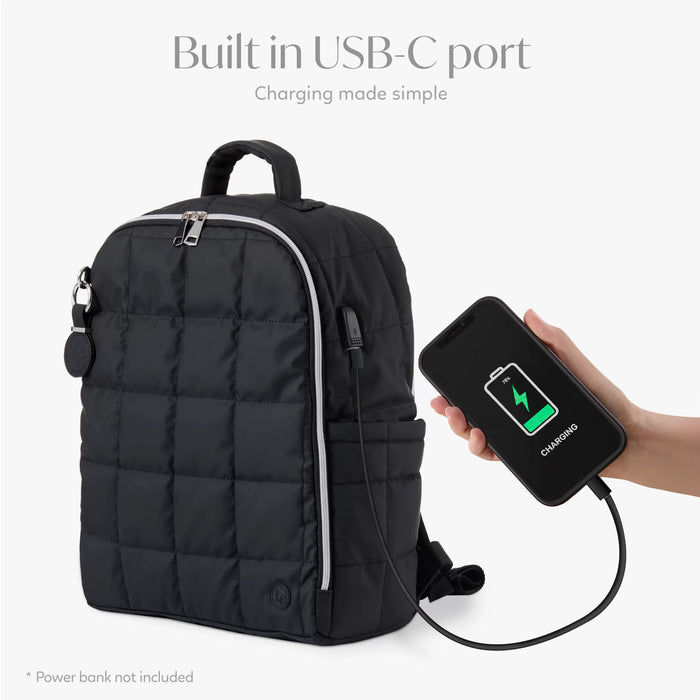 Black quilted backpack with built-in USB-C port charging a smartphone, white background