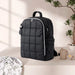 Black quilted diaper backpack on table with baby bottle, pacifier, and patterned cloth nearby