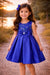 Navy blue party dress for girls with bow detail, shown outdoors at sunset.