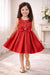 Red party dress for girls with floral embroidery and bow, modeled indoors in a bright room.