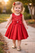 Red party dress with bow and floral details, shown on a smiling toddler outdoors on a walkway.