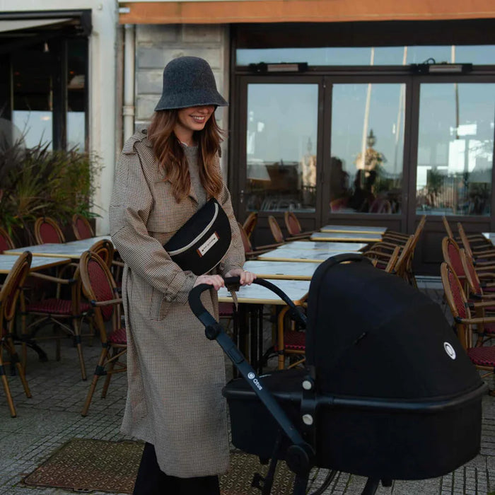 Black stroller shown outdoors by a woman in a coat and hat, next to a patio café.