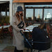 Black stroller shown outdoors by a woman in a coat and hat, next to a patio café.