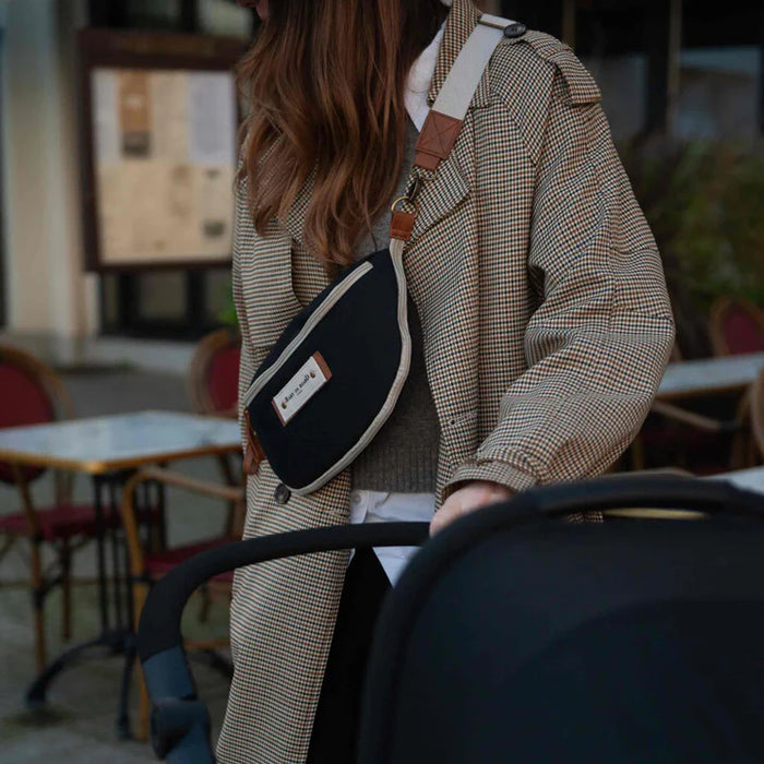 Black crossbody diaper bag worn by a woman pushing a stroller outdoors.