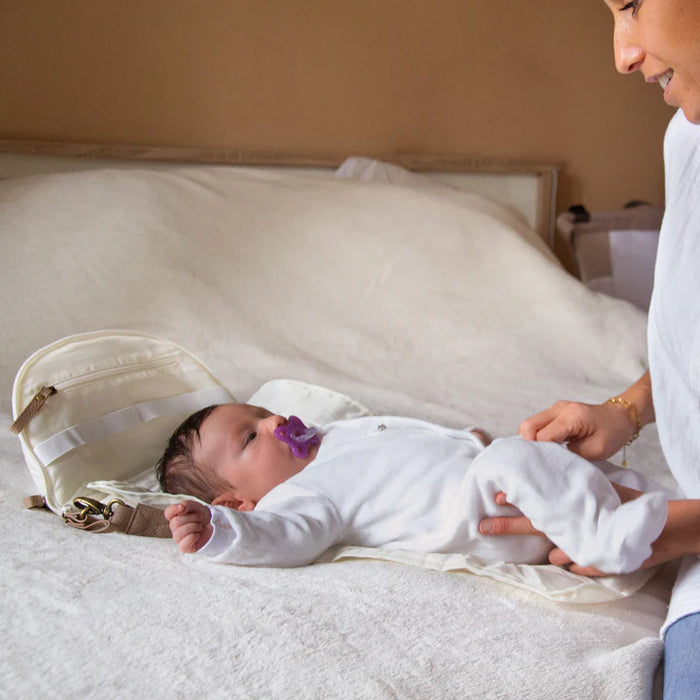 Portable baby changing pad with baby lying on bed, parent holding baby's legs gently.