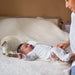 Portable baby changing pad with baby lying on bed, parent holding baby's legs gently.
