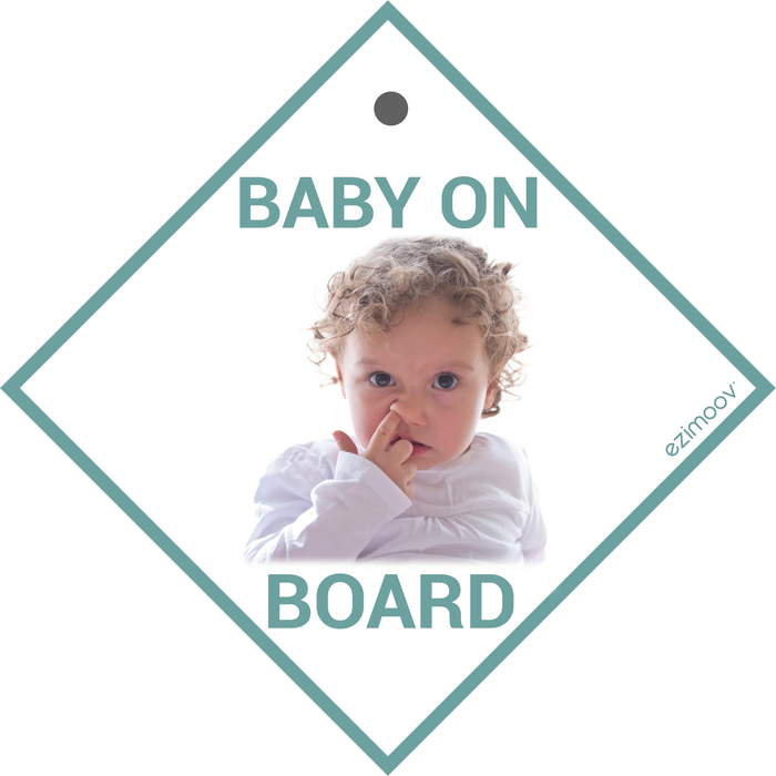 EziMoov Baby on Board car sign featuring a baby with curly hair, picking nose, on a white background.