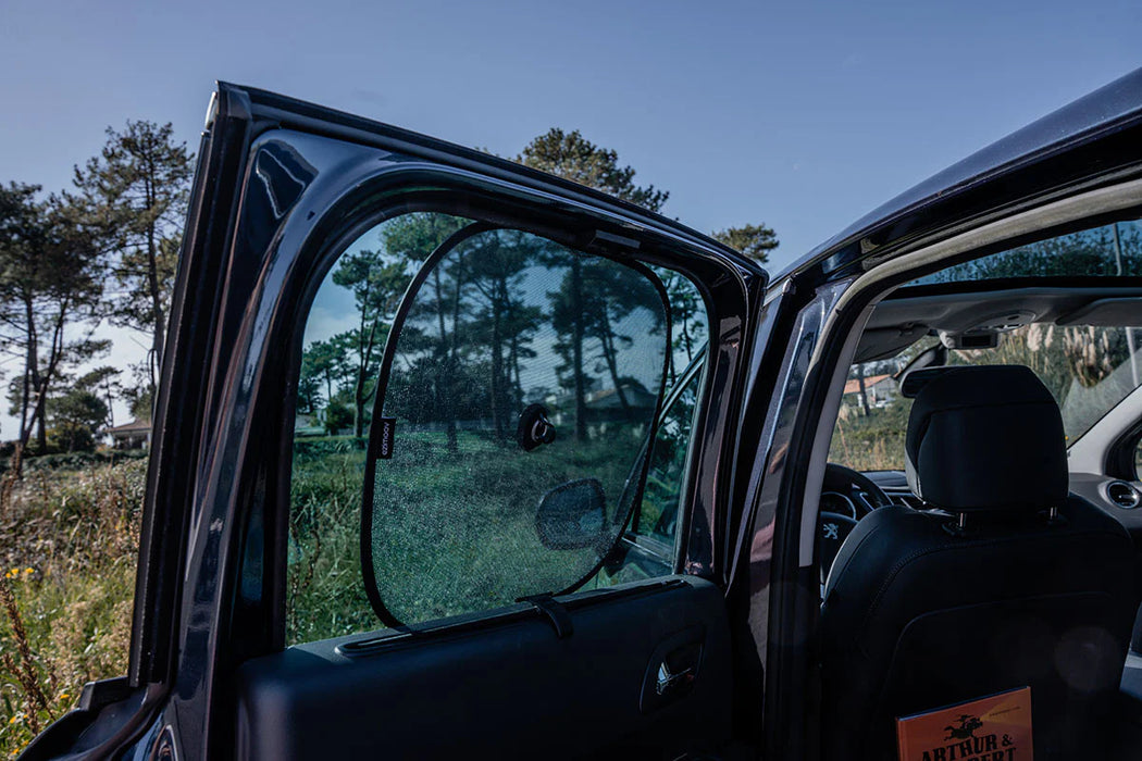 Car window sunshade installed on rear door, viewed outdoors with trees in the background.