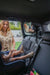 A rear-facing baby car seat with a child and a safety mirror attached to the car's backseat headrest.