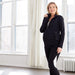 Maternity active jacket shown on a pregnant woman standing in a bright room with large windows.