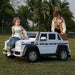 Kids ride-on white toy SUV car with two children playing on it outdoors on grassy field.