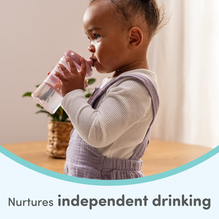 Toddler using a pink sippy cup at a table, encouraging independent drinking skills.