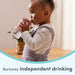 Toddler using a pink sippy cup at a table, encouraging independent drinking skills.