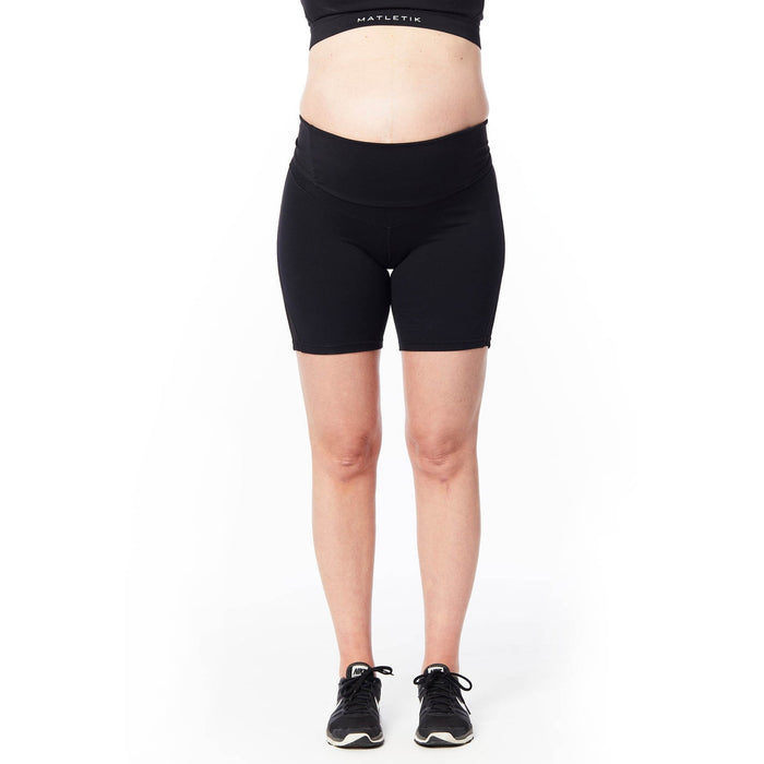 MATLETIK black maternity biker shorts worn by a pregnant model standing on a white background.