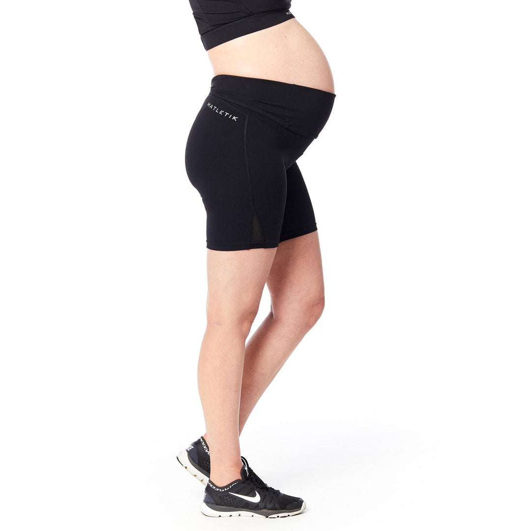 Matletik black maternity biker shorts worn by a pregnant woman standing in profile on white background.