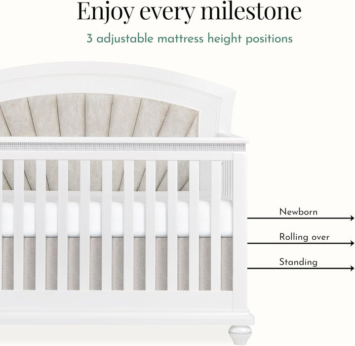 White baby crib with tufted fabric headboard and height-adjustable mattress positions