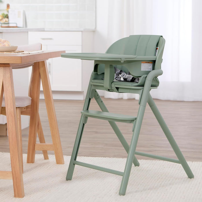 Sage green baby high chair with safety harness in modern kitchen setting