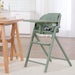 Sage green baby high chair with safety harness in modern kitchen setting