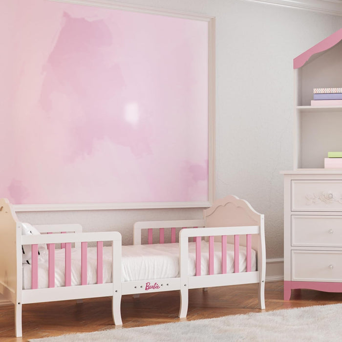 Pink and white toddler bed with Barbie logo in a girl's nursery with dresser and bookshelf