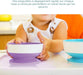 Silicone suction bowl for babies in purple, held by a child at a high chair during mealtime.