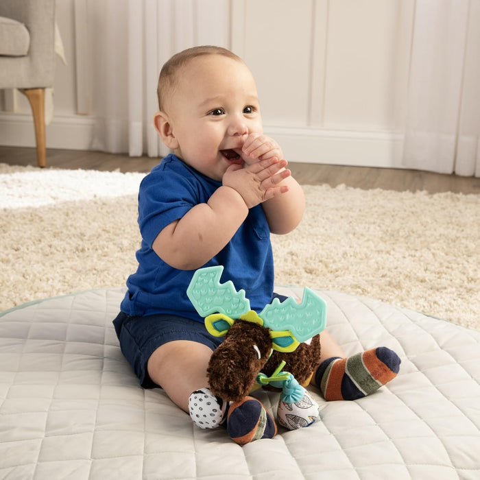 Baby wearing a blue shirt playing with a plush moose toy on a quilted play mat indoors.