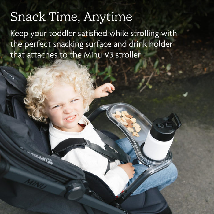 Toddler sitting in stroller with snack tray and drink holder outdoors