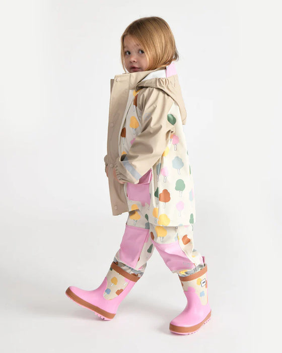 Kids rain jacket with pastel tree print, modeled by a child in matching rain pants and pink boots