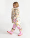 Kids rain jacket with pastel tree print, modeled by a child in matching rain pants and pink boots