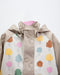 Children's rain jacket with colorful tree print, beige sleeves, and snap buttons shown on display.