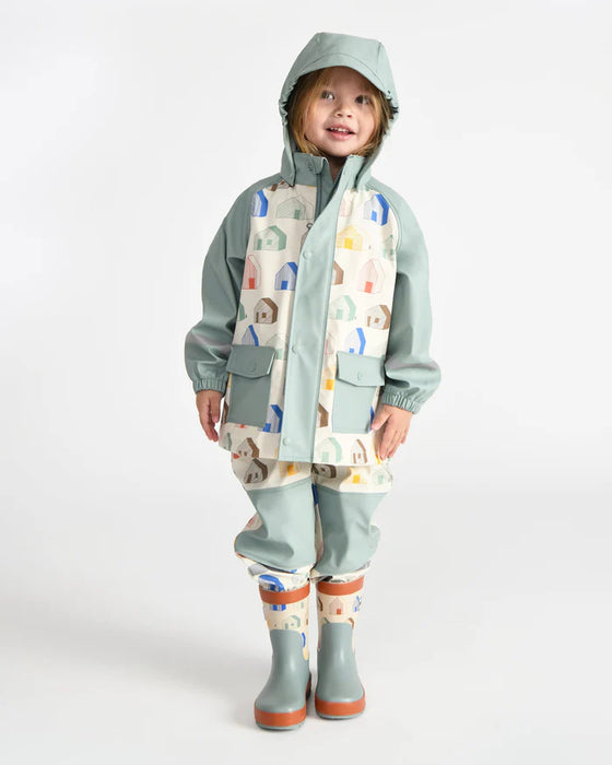 Kids rain jacket with pastel house print shown on a child standing against a white background.