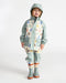 Kids rain jacket with pastel house print shown on a child standing against a white background.