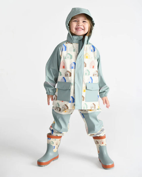 Kids rain jacket and pants set with pastel house print, shown on a smiling child in boots