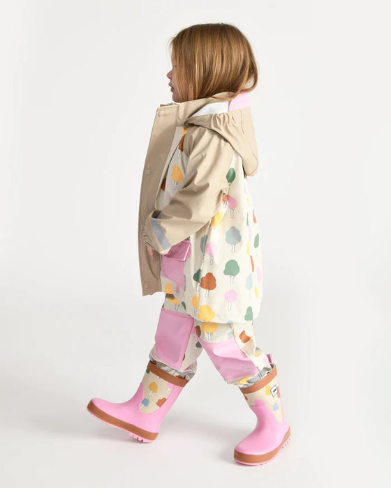 Child wearing a colorful rain jacket, patterned pants, and pink rain boots walking indoors.