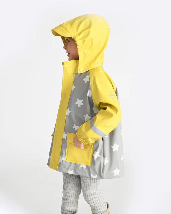 Child wearing a 7AM rain jacket in yellow and grey with star pattern, standing sideways.