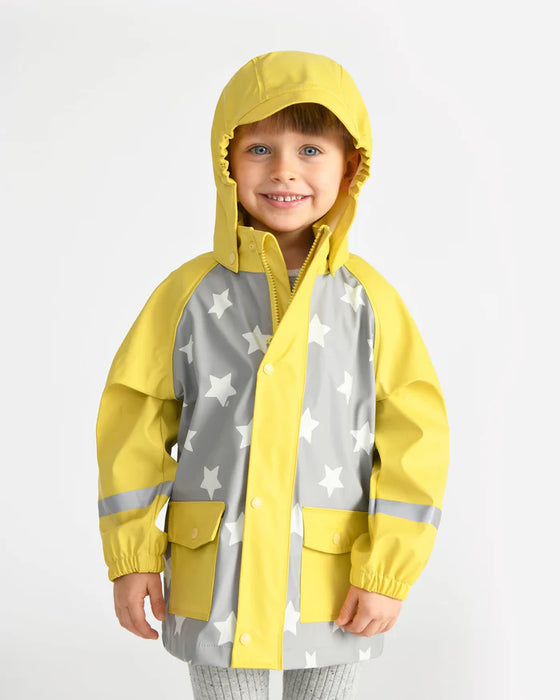 Kids rain jacket with yellow hood and sleeves, gray body with white stars, modeled by a child indoors.