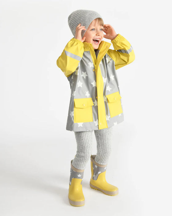 Kids rain jacket with yellow and grey star pattern, worn by a child standing and smiling indoors.