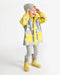 Kids rain jacket with yellow and grey star pattern, worn by a child standing and smiling indoors.