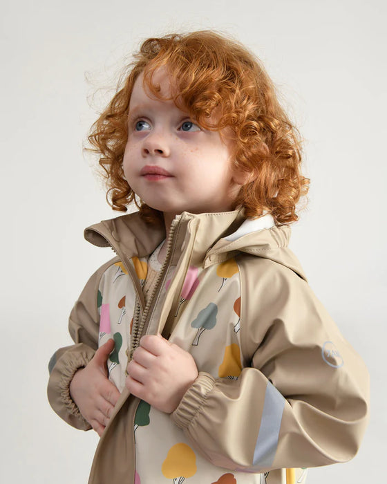 7AM rain jacket in beige with colorful tree print, worn by a young child facing upward indoors.
