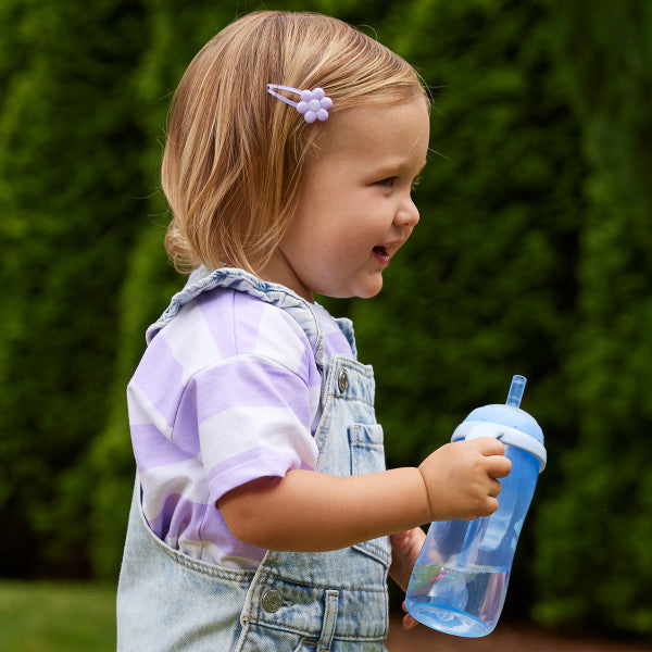 Toddler holding a blue sippy cup outdoors, wearing striped shirt and denim overalls.