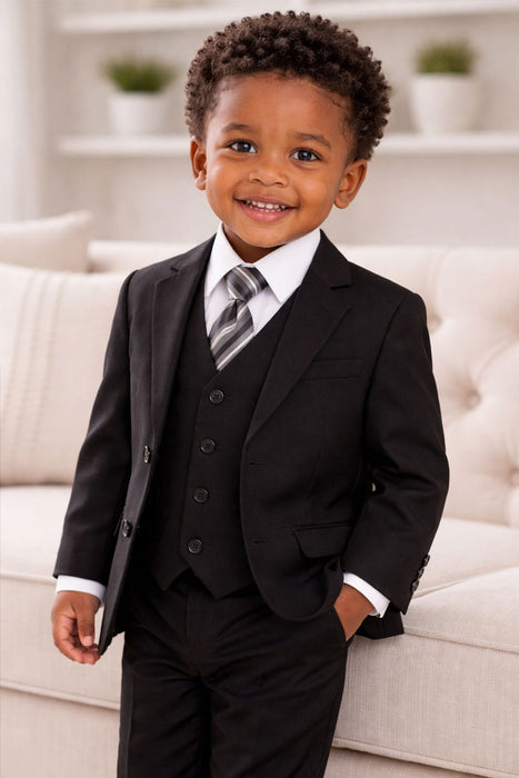 Toddler in a black suit, white dress shirt, striped tie, and vest, smiling indoors