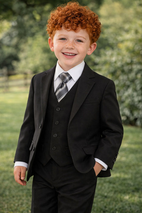 Smiling young boy in black suit with striped tie standing outdoors